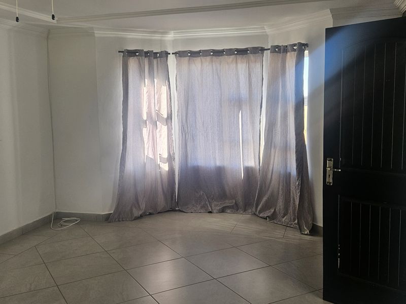 A bright, empty living room featuring large bay windows, neutral tiled flooring, and clean white walls, offering a versatile space for interior design.