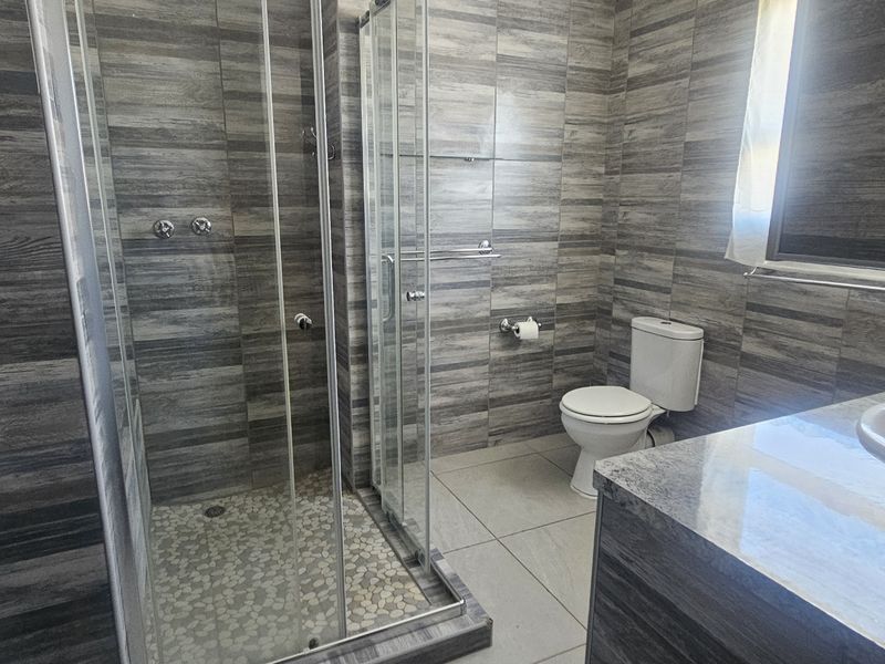 Modern bathroom featuring a glass-enclosed shower with pebble flooring, a vanity basin, and contemporary stone-look wall tiles.