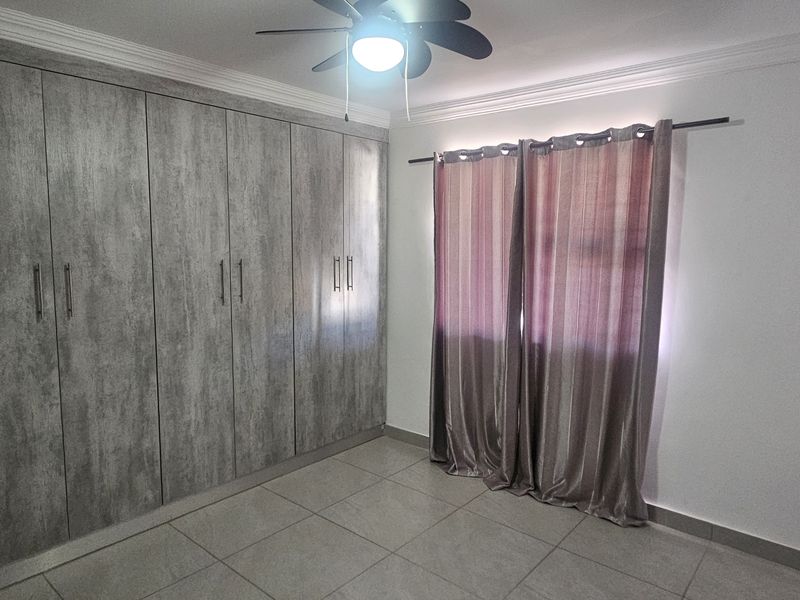 A clean, empty bedroom featuring modern grey built-in cupboards, tiled flooring, and a ceiling fan, offering a neutral space ready for personalization.