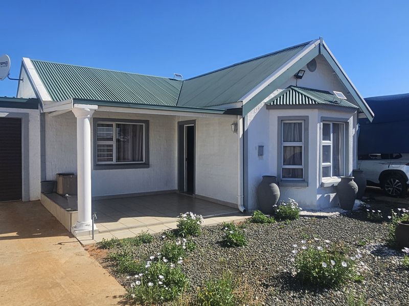 Front elevation of a single-story house featuring a corrugated metal roof, a tiled porch with a column, a bay window, and an attached garage.