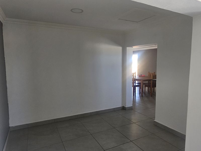 An empty living area featuring neutral tiled flooring, recessed lighting, and coving, providing a blank canvas for interior design.