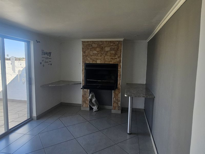 An indoor entertainment area featuring a built-in braai with stone cladding, tiled flooring, and a sliding glass door leading to an outdoor patio.