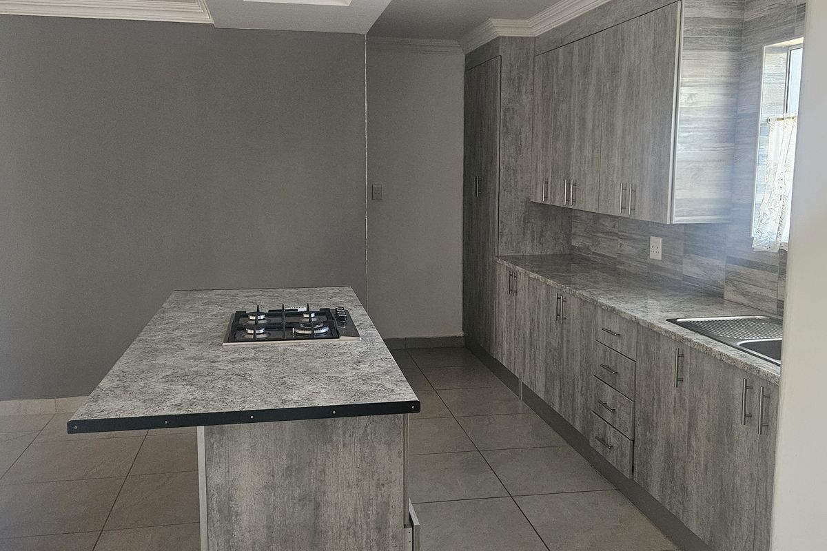 Modern kitchen featuring grey wood-look cabinetry, laminate countertops, a central island with a gas hob, and tiled flooring.