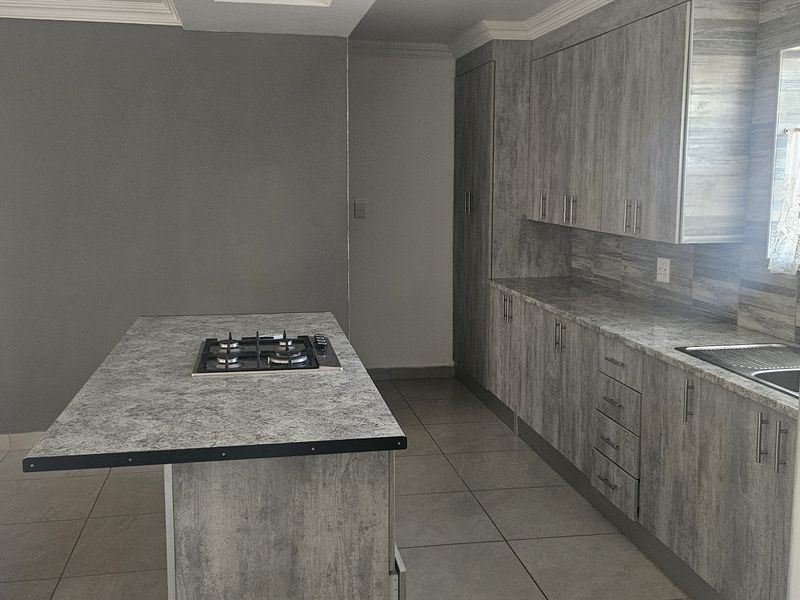 Modern kitchen featuring grey wood-look cabinetry, laminate countertops, a central island with a gas hob, and tiled flooring.