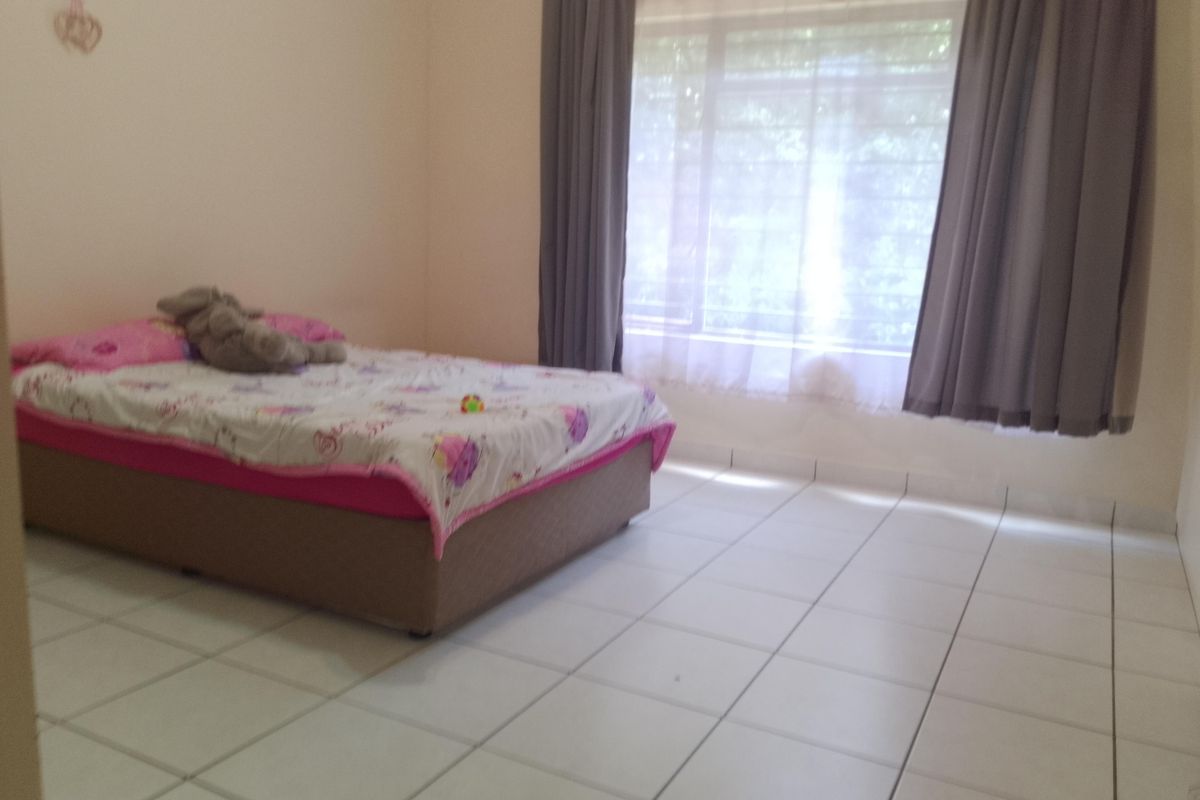 A simple bedroom featuring neutral tiled flooring and a large window with curtain tracks, providing natural light to the space.