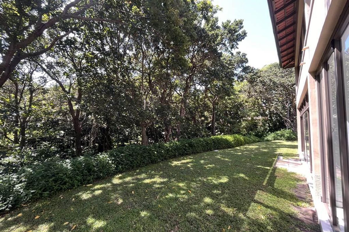 A private rear garden area featuring a well-maintained lawn, mature trees, and direct access to the apartment through large sliding glass doors.
