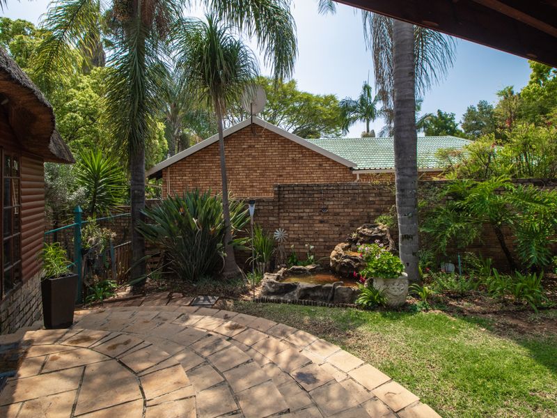A private rear garden featuring a stone paved patio, established landscaping, and a built-in water feature, viewed from a covered outdoor area.
