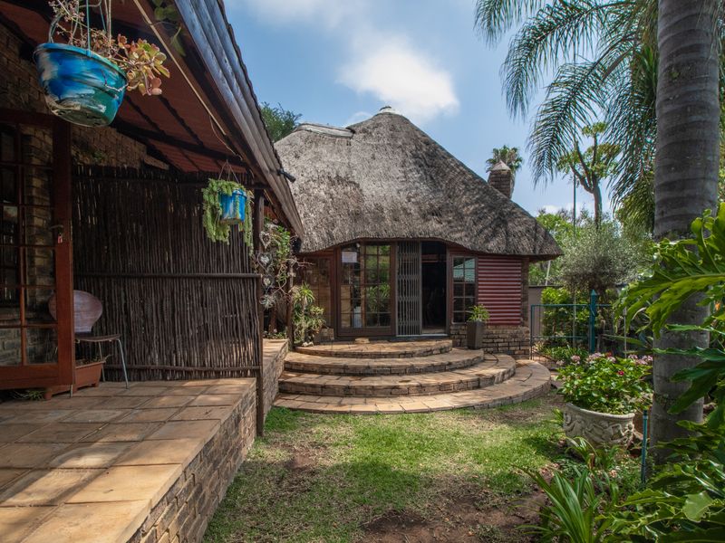 A charming rear exterior view featuring a traditional thatch roof, curved brick steps leading to the entrance, and a paved patio area.