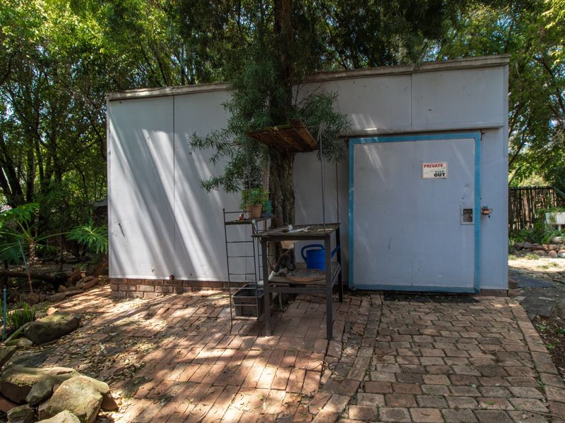 A detached utility structure featuring metal cladding and a brick-paved exterior area, situated in a garden setting.