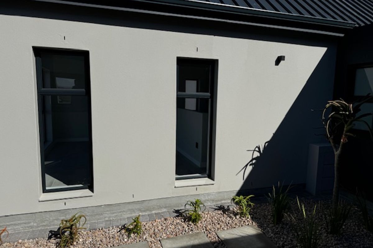 A modern exterior rear elevation featuring clean rendered walls, dark aluminium window frames, and a neatly landscaped garden area with stone paving.