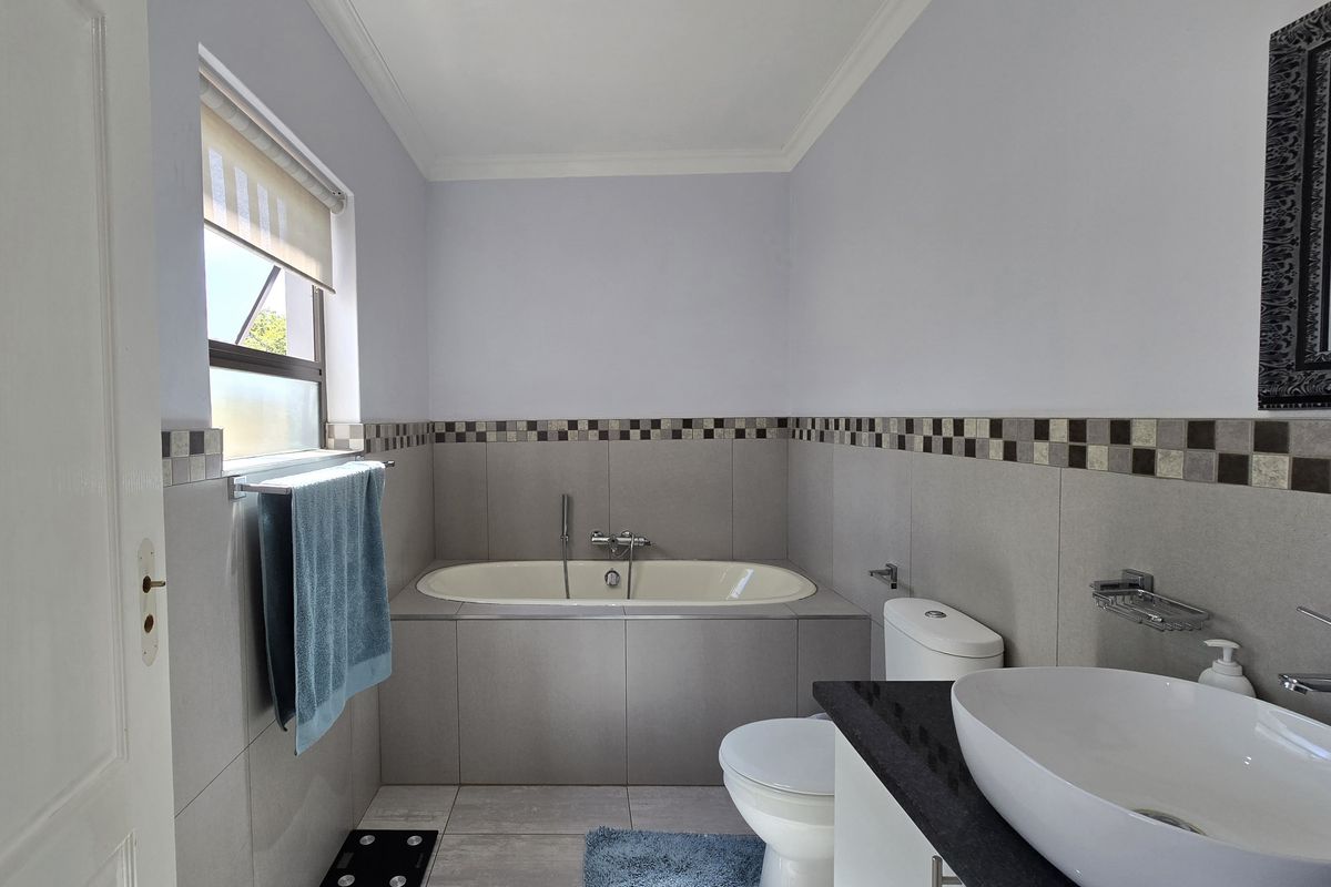 A well-maintained bathroom featuring a built-in bathtub, a modern countertop basin on a vanity cabinet, and neutral ceramic tiling throughout.