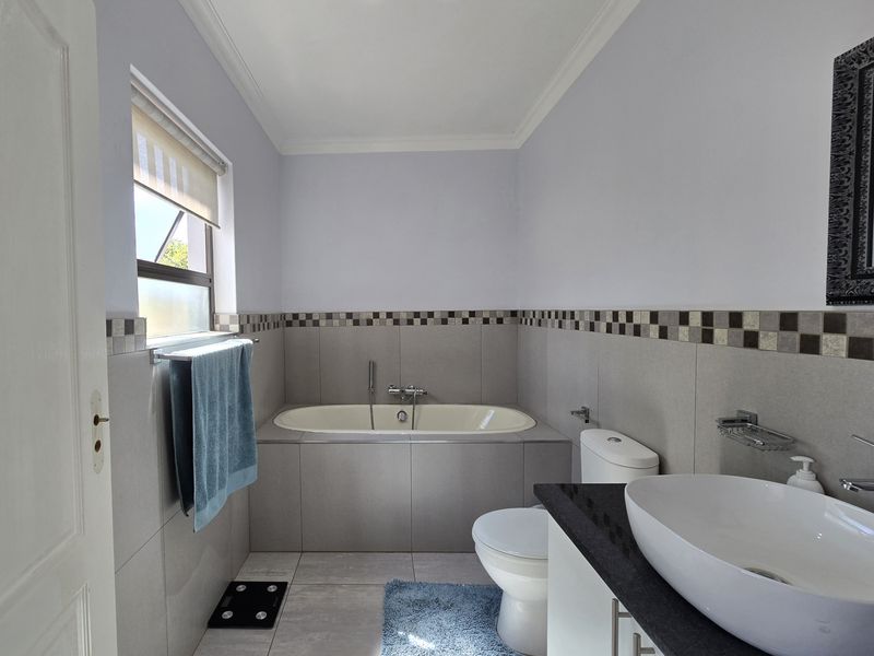 A well-maintained bathroom featuring a built-in bathtub, a modern countertop basin on a vanity cabinet, and neutral ceramic tiling throughout.
