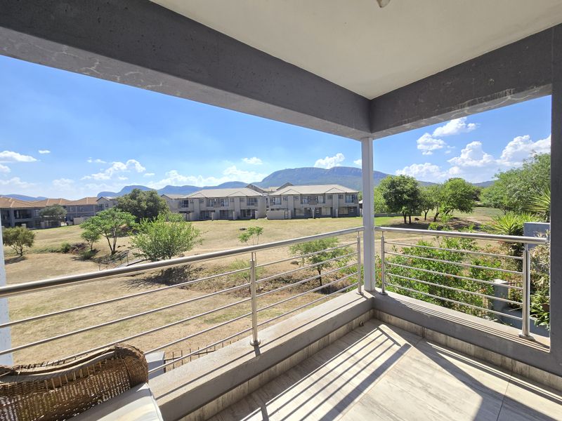 A covered balcony featuring tiled flooring and a stainless steel balustrade, offering expansive views of the surrounding estate and mountain landscape.