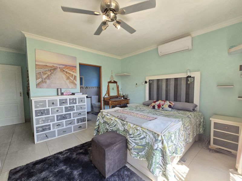 A bedroom featuring tiled flooring, a ceiling fan, and a wall-mounted air conditioning unit, with direct access to an en-suite bathroom.