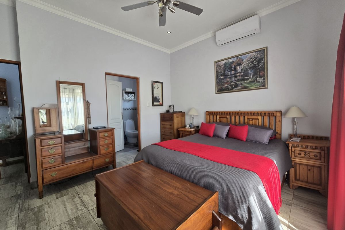 Spacious bedroom featuring tiled flooring, a ceiling fan, and a wall-mounted air conditioning unit, with convenient access to an en-suite bathroom.