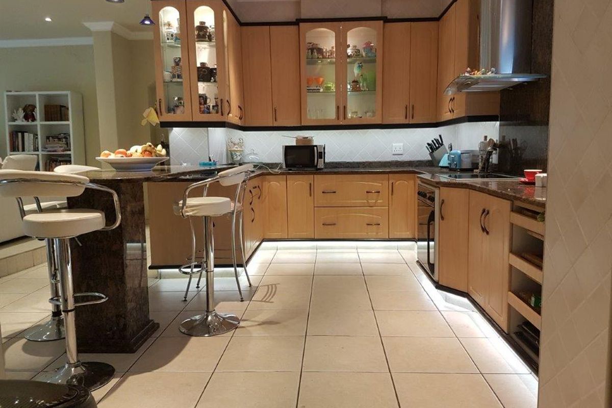 A well-lit kitchen featuring light wood cabinetry, granite countertops, a breakfast bar, and tiled flooring with integrated under-cabinet lighting.