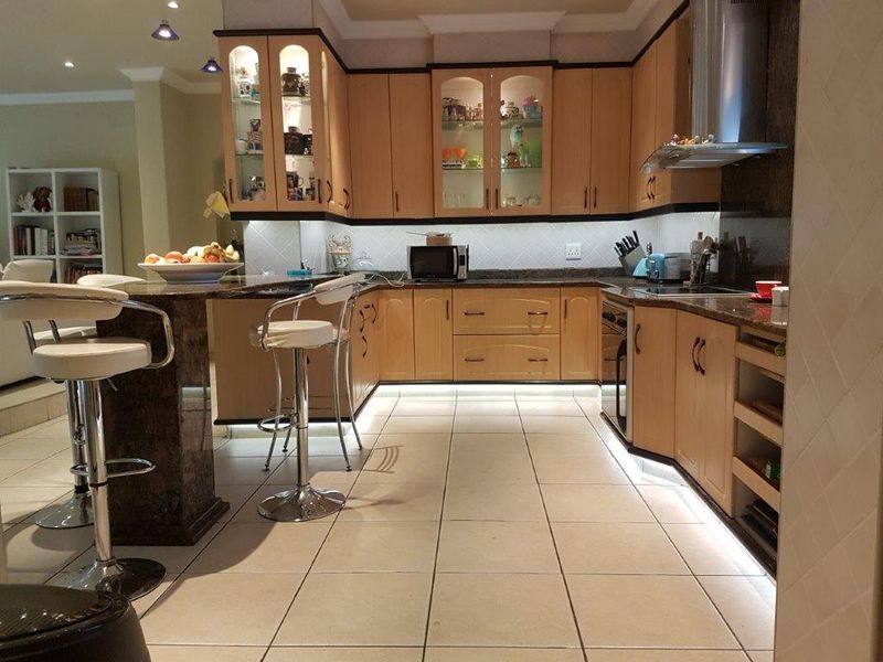 A well-lit kitchen featuring light wood cabinetry, granite countertops, a breakfast bar, and tiled flooring with integrated under-cabinet lighting.