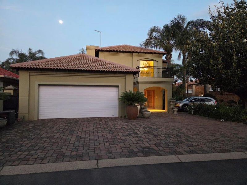 Front elevation of a double-story house featuring a tiled roof, paved driveway, double garage, and an upper-level balcony with wrought iron railings.