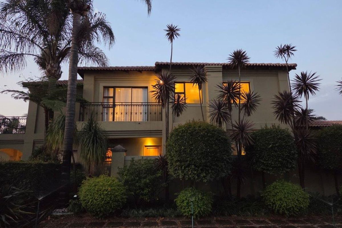 A well-maintained two-story residential exterior featuring a balcony with wrought iron railings, tiled roofing, and established garden landscaping at dusk.