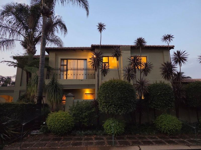 A well-maintained two-story residential exterior featuring a balcony with wrought iron railings, tiled roofing, and established garden landscaping at dusk.