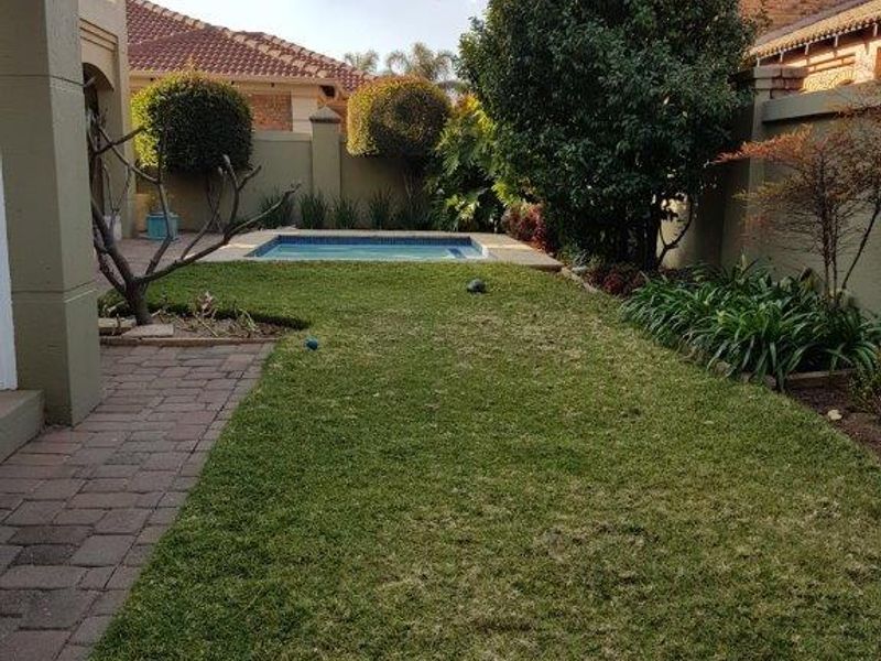 A well-maintained rear garden featuring a paved walkway, established landscaping, and a private swimming pool enclosed by boundary walls.