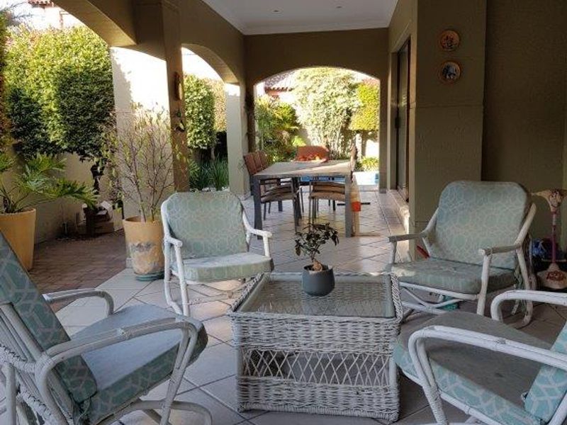 A spacious covered patio area featuring tiled flooring, recessed lighting, and arched structural pillars, providing a comfortable outdoor living and dining space.