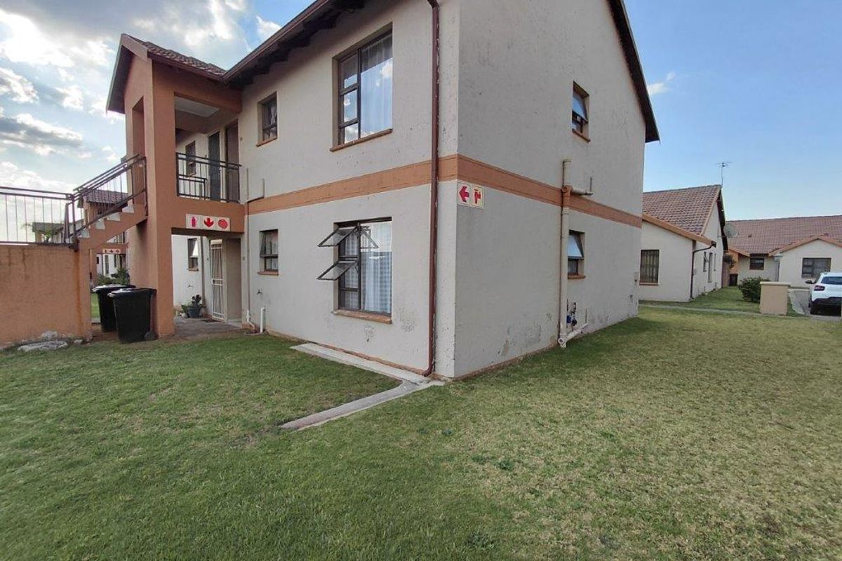 Exterior view of a two-story apartment building showing rear facade, staircase access, and surrounding lawn area.
