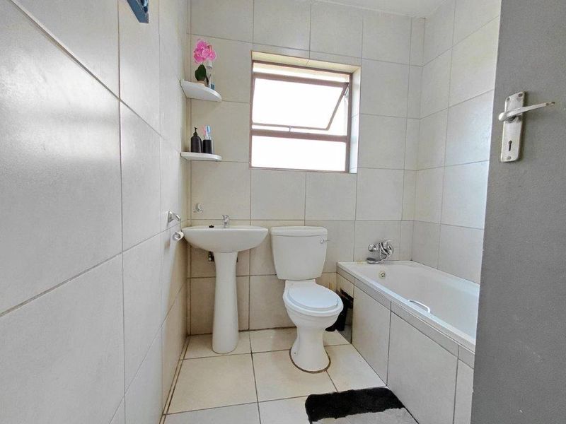 A functional bathroom featuring a pedestal washbasin, toilet, and bathtub with full-height wall tiling and a casement window for natural ventilation.