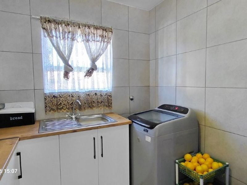 A functional laundry area featuring tiled walls, a stainless steel sink with a wooden countertop, and built-in white cabinetry.