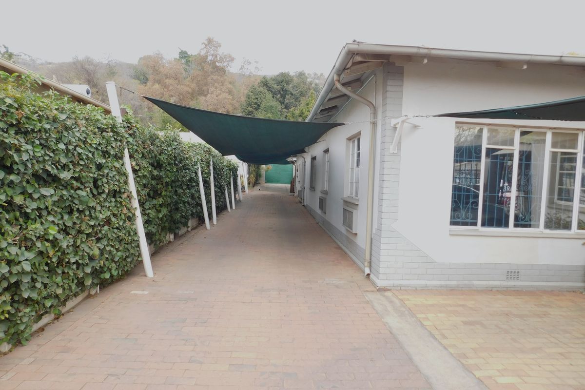 A paved side driveway area featuring a shade sail, brick exterior walls, and security bars on the windows.