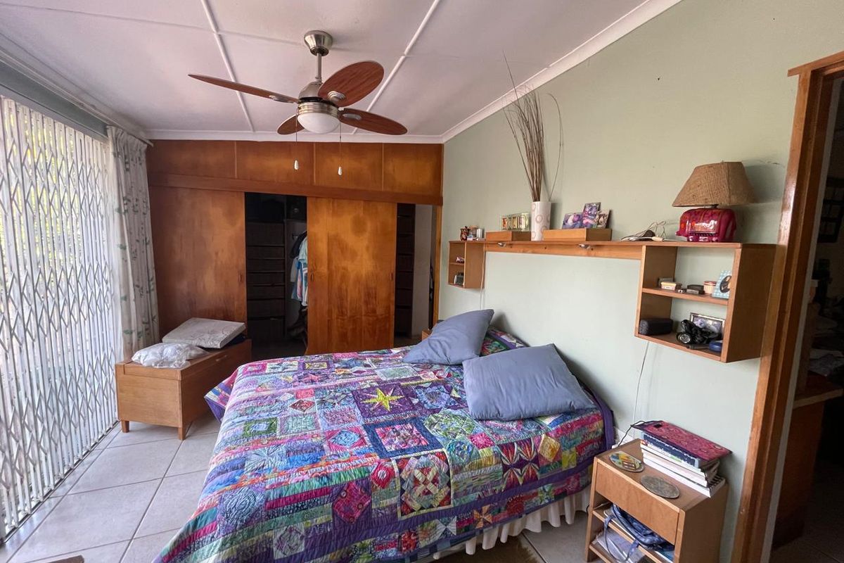 A bedroom featuring built-in wooden cupboards, a ceiling fan, tiled flooring, and a sliding security gate leading to the exterior.