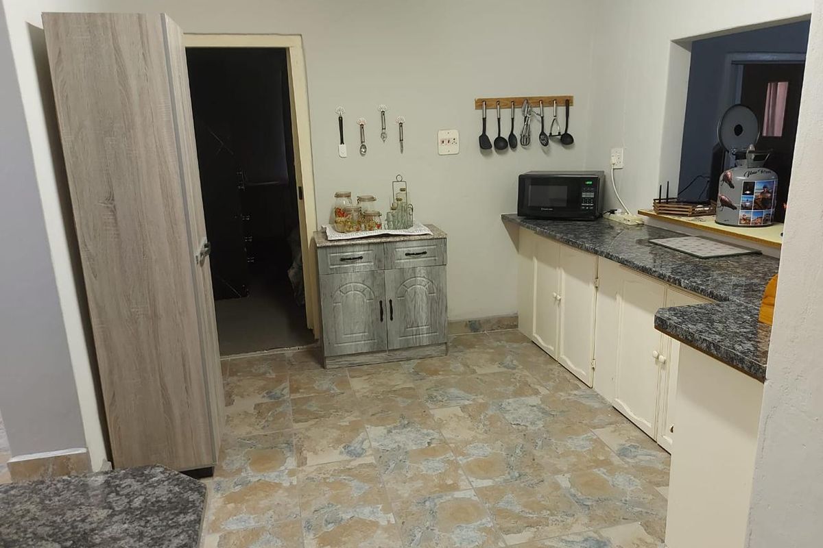 A functional kitchen area featuring granite countertops, tiled flooring, and built-in cabinetry with a mix of wood-grain and painted finishes.