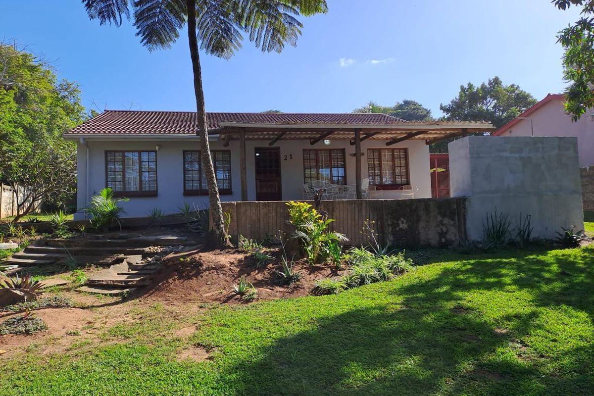 Rear view of the house featuring a covered patio, timber pergola, stone steps, and an unfinished masonry braai structure set within a landscaped garden.