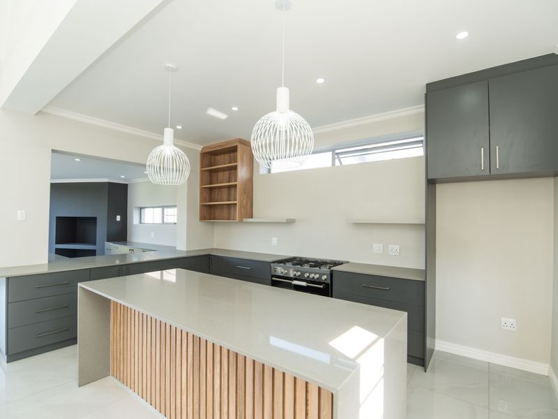 Modern kitchen featuring a large island with quartz countertops, sleek grey cabinetry, gas stove, and contemporary pendant lighting in an open-plan layout.