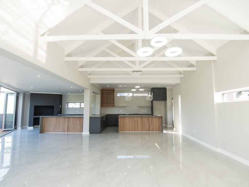 Spacious open-plan living and kitchen area featuring vaulted ceilings with exposed trusses, modern cabinetry, a kitchen island, and large bi-fold doors leading outdoors.