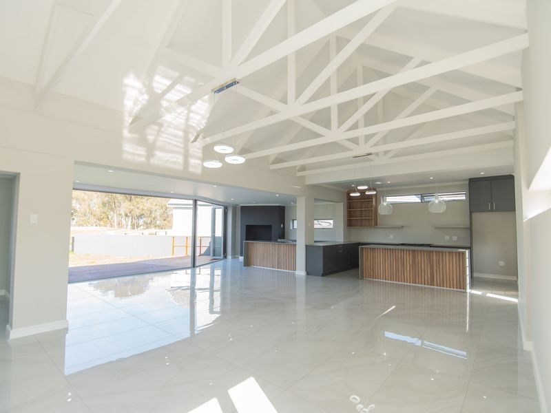 Spacious open-plan living and kitchen area featuring high vaulted ceilings with exposed trusses, modern cabinetry, and large sliding doors leading to the outdoors.