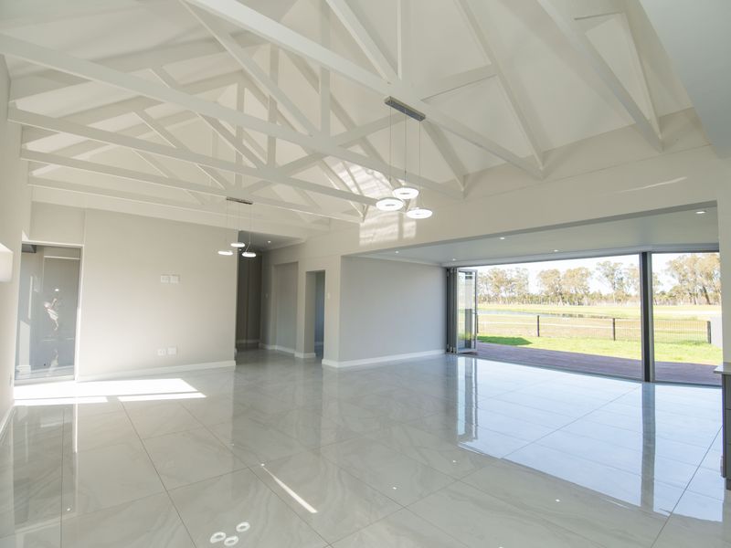 Spacious open-plan living area featuring high vaulted ceilings with exposed white trusses, polished porcelain tiles, and seamless access to the outdoor patio.