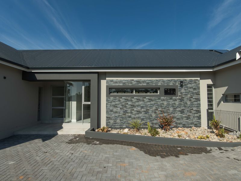 Modern front facade featuring a corrugated metal roof, stone cladding accents, a paved driveway, and a glass entrance door.