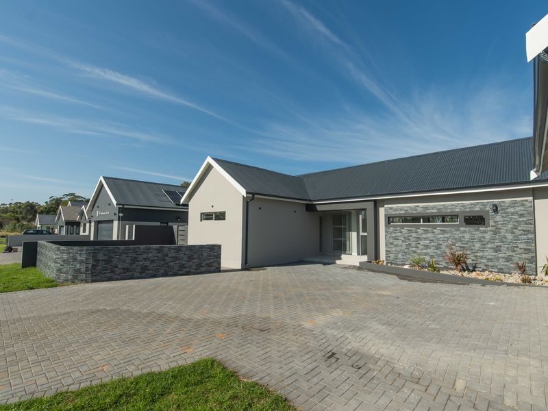 Modern front elevation featuring a paved driveway, stone cladding accents, and a contemporary metal roof design.