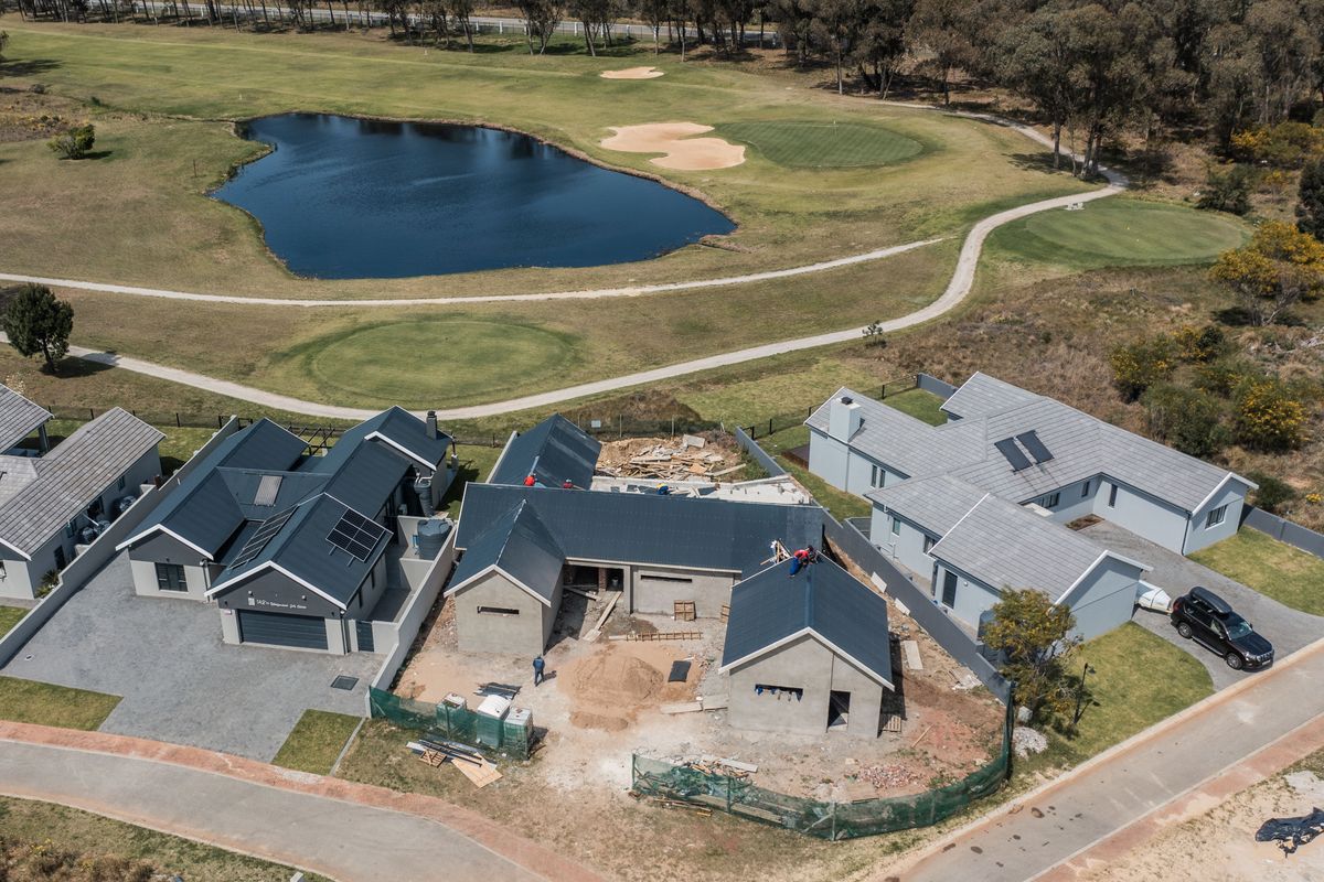 Aerial view of a residential property under construction, featuring multiple roof structures, solar panels, and proximity to a golf course and water feature.