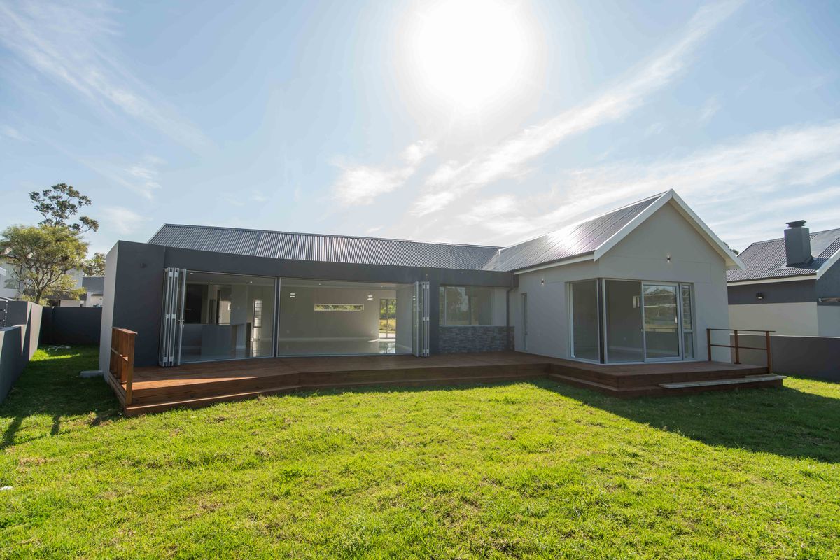 Rear view of a modern house featuring extensive timber decking, large bi-fold doors, and a well-maintained lawn area.