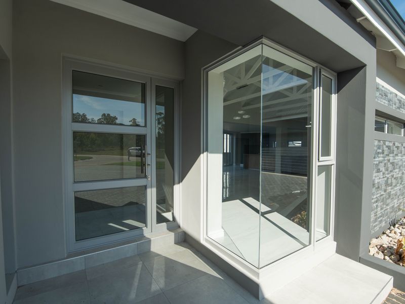 Modern front entrance featuring a glass door, corner window, stone cladding accents, and a clean tiled porch area.
