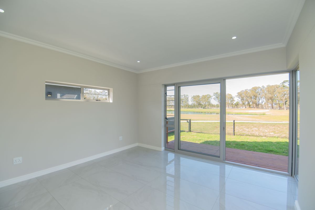 A bright, empty living room featuring large sliding glass doors that open onto a deck, with modern porcelain floor tiles and recessed lighting.