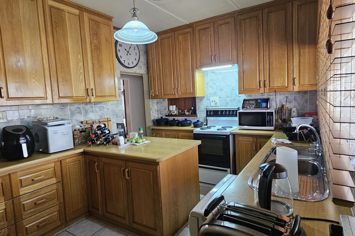 A functional kitchen featuring traditional wooden cabinetry, laminate countertops, a tiled backsplash, and a freestanding stove with an integrated extractor fan.