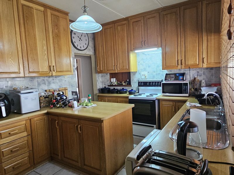 A functional kitchen featuring traditional wooden cabinetry, laminate countertops, a tiled backsplash, and a freestanding stove with an integrated extractor fan.