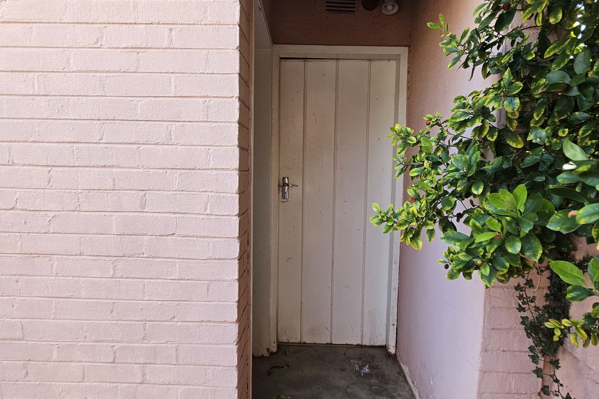 A side or rear exterior access point featuring a painted brick wall, a timber door, and concrete flooring.