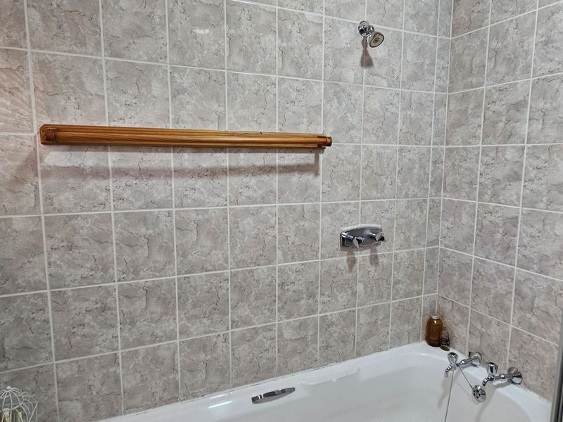 A functional bathroom featuring a bathtub with a shower head, tiled walls, and a wooden towel rail.