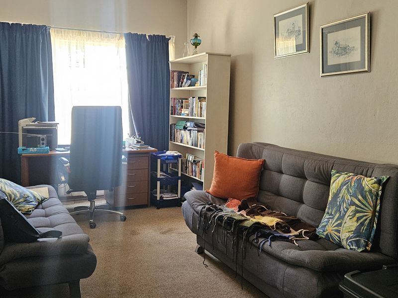 A functional living room space featuring carpeted flooring and natural light from the window, suitable for a comfortable lounge or home office area.