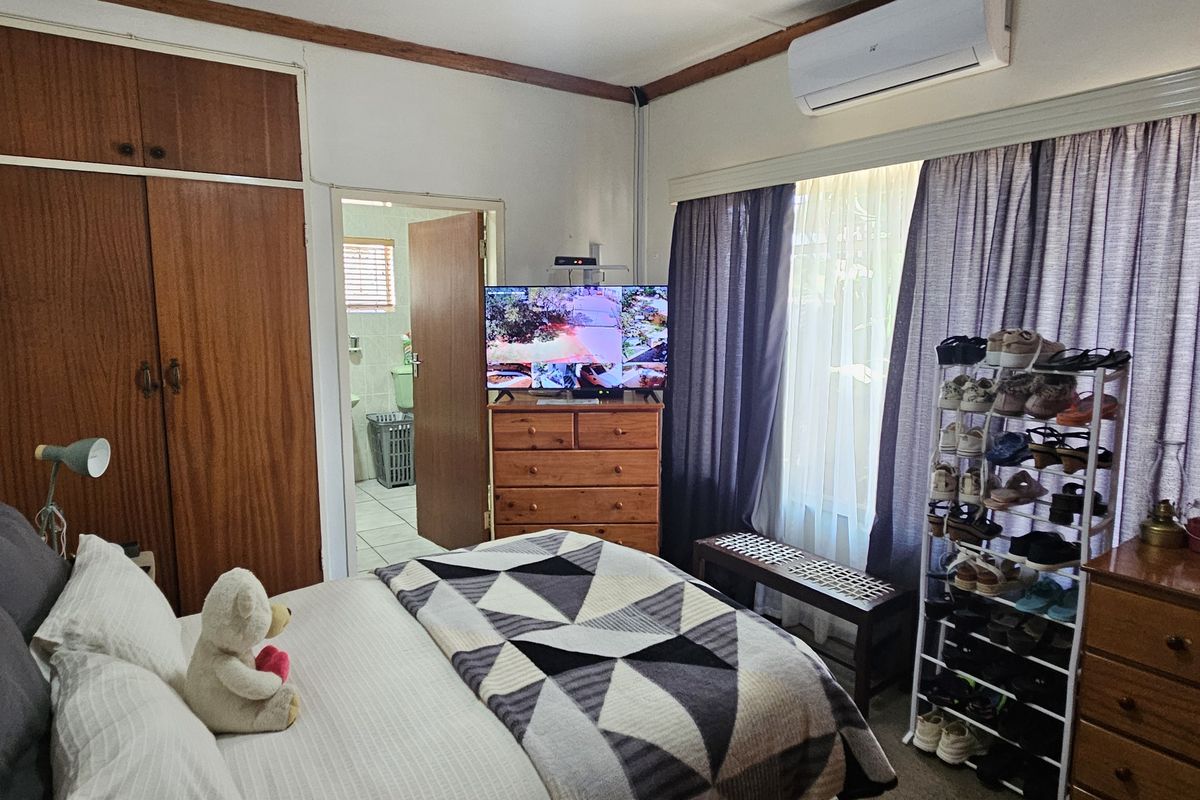 A functional bedroom featuring built-in wooden cupboards, a wall-mounted air conditioning unit, and direct access to an en-suite bathroom.