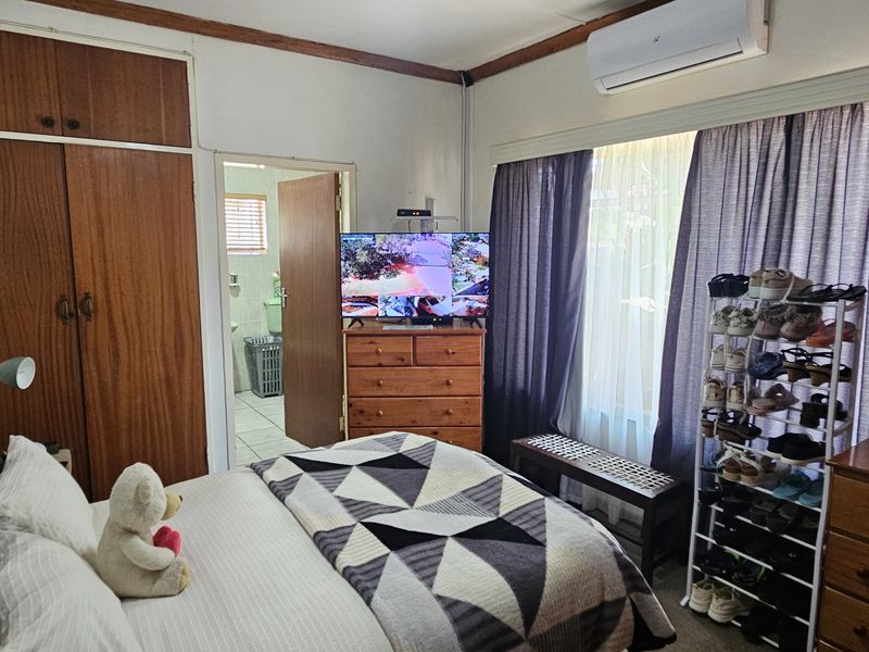 A functional bedroom featuring built-in wooden cupboards, a wall-mounted air conditioning unit, and direct access to an en-suite bathroom.